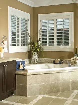 Bathroom with a tub plants and window shutters Bathroom with a tub, plants, and window shutters